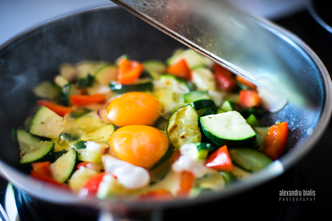 Fotografie culinara, zucchini, oua ochi, ardei rosu, ceapa verde in tigaie, gatite al dente