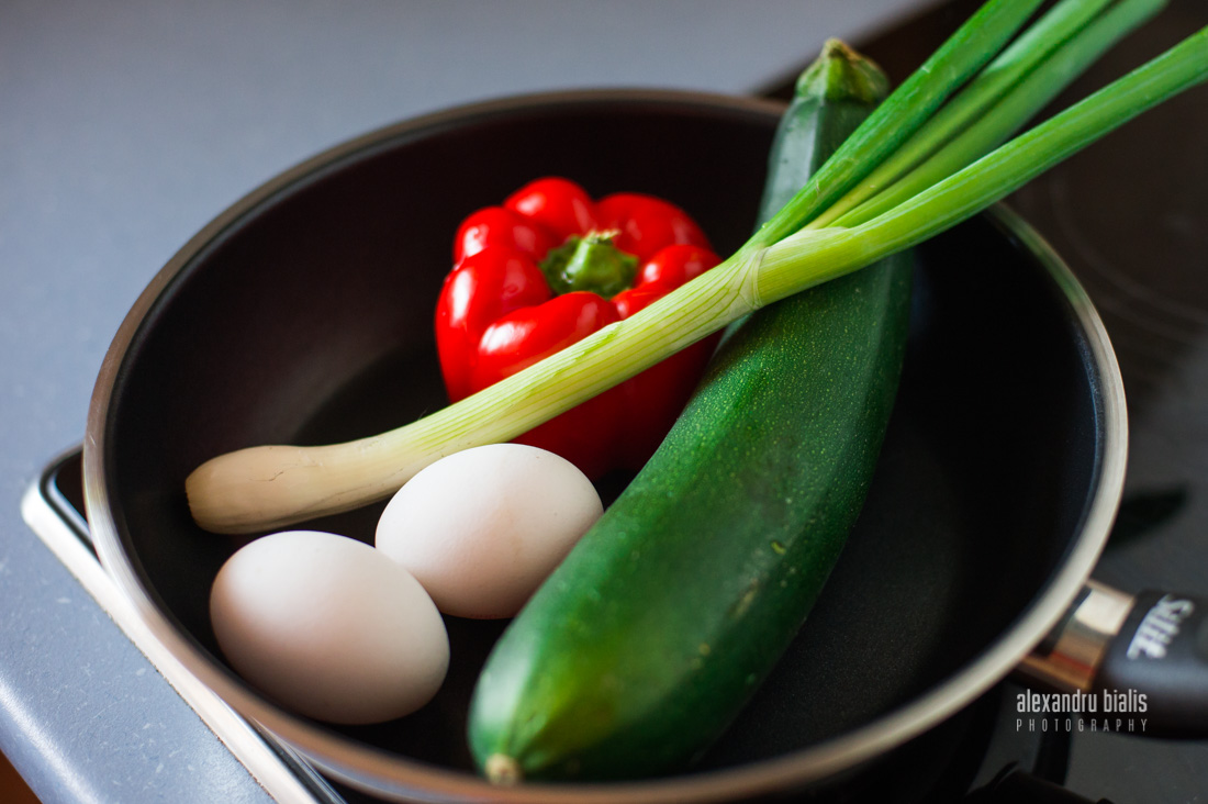 Fotografie culinara, zucchini, oua crude, ardei rosu, ceapa verde in tigaie